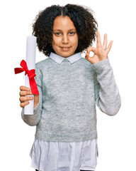 Sticker - Young little girl with afro hair holding graduate degree diploma doing ok sign with fingers, smiling friendly gesturing excellent symbol