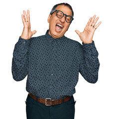 Sticker - Middle age indian man wearing casual clothes and glasses celebrating mad and crazy for success with arms raised and closed eyes screaming excited. winner concept