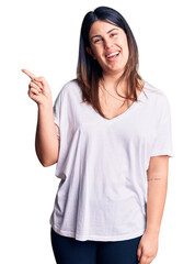 Wall Mural - Young beautiful brunette woman wearing casual t-shirt with a big smile on face, pointing with hand and finger to the side looking at the camera.