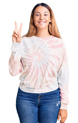 Sticker - Beautiful young woman wearing casual tie dye sweatshirt smiling with happy face winking at the camera doing victory sign. number two.