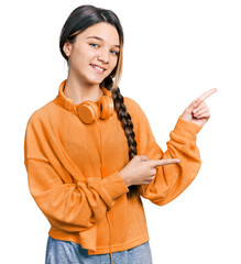 Wall Mural - Young brunette girl with long hair wearing sweatshirt and headphones smiling and looking at the camera pointing with two hands and fingers to the side.