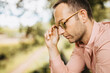 © Shotmedia - summer portrait of young man in pink shirt with hands on sunglasses while being outside in park and enjoy the carefree time