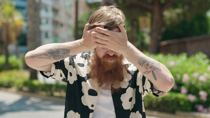 Wall Mural - Young redhead man taking off shirt sweating at park