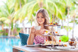 © TravelMedia - Woman drink coffee or tea with desserts at restaurant with palm trees