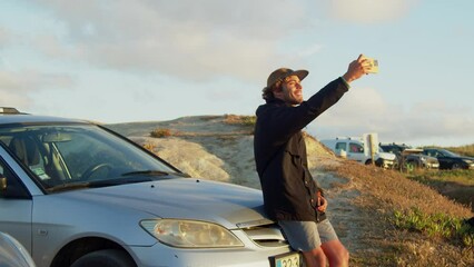 Wall Mural - Curly male person sitting at the car hood and making self portrait