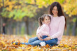 Happy mother and daughter in the autumn park. Beauty nature scene with family outdoor lifestyle. Happy family resting together on green grass, having fun outdoor. Happiness and harmony in family life