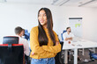 © baranq - Young Asian female entrepreneur standing at coworking office. Portrait of smiling businesswoman in startup office