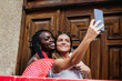 two women friends of different ethnicity take a selfie in the street during the popular festivities of a town in spain. concept of fun, friendship and diversity.