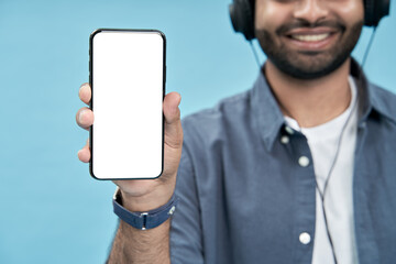 Happy smiling young man student wearing headphones showing cellphone big mockup white blank phone template screen isolated on blue background presenting smartphone mobile app offer ads. E learning.