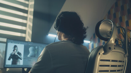 Wall Mural - man in headphones creating video game character in 3d modeling program while sitting at the table at
