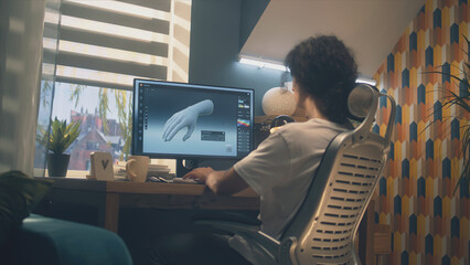Wall Mural - male designer sitting on chair at the table at home office and making 3d prototype of human hand in 