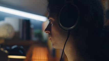 Wall Mural - man in headphones browsing the internet and social networks on computer at home at night and listeni