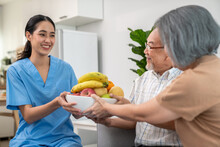 Contented Senior Couple Taking A Bowl Of Fruit From A Nurse At Home. Senior Care At Home.