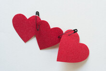Three Red Fabric Hearts Joined Together With Black Safety Pins On Blank Paper (version 1)