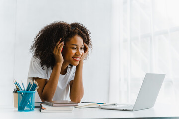 Wall Mural - Young pretty african amerian woman studying online with laptop at living room.