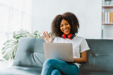 Wall Mural - Young pretty african amerian woman studying online with laptop at living room.