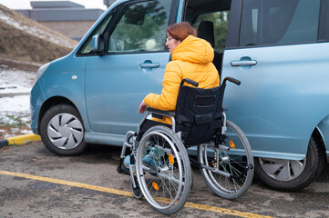 Caucasian woman in a wheelchair gets into the car. 