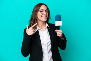 Wall Mural - Young TV presenter woman isolated on blue background giving a thumbs up gesture