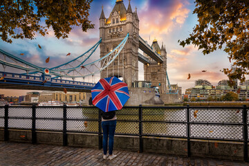 Wall Mural - London in autumn time concept with a tourist person holding a british flag umbrella in front of the famous Tower Bridge during sunset time