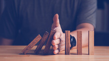 Risk Assessment And Management Concept. Man's Hand Prevent Or Protect The Domino Wood Block Like Risk That Will Impact Or Effect Their Business With Good Risk Assessment.