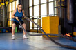 Active old woman in sportswear training with battle rope in cross fit gym
