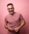 Successful pleased european bearded mature man, standing and smiling broadly, wearing glasses and t-shirt over pink background. handsome man with with crossed arms looking at the camera. positive male