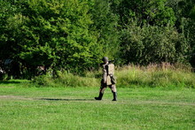 A Close Up On A Single Soldier In A Complete Outfit, With Helmet, Backpack, And A Gun On His Shoulder Traversing A Small Path In The Middle Of A Field To Reach A Nearby Forest Or Moor In Poland