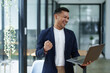 © Jirapong - Portrait of an Asian male business owner standing with a computer showing happiness after a successful investment