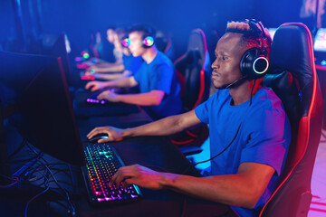 Wall Mural - Streamer african young man with team rejoices in victory professional gamer playing online games computer with headphones, neon color