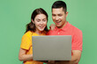 © ViDi Studio - Young smiling happy cheerful fun IT couple two friends family man woman in basic t-shirts together hold use work on laptop pc computer isolated on pastel plain light green background studio portrait
