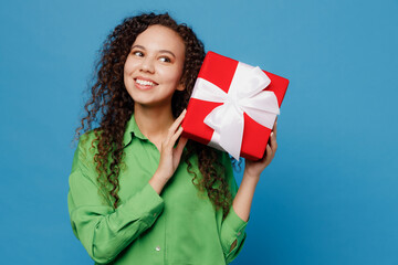 Wall Mural - Young minded woman of African American ethnicity 20s wear green shirt hold red present box with gift ribbon bow look aside isolated on plain blue background studio portrait. People lifestyle concept.