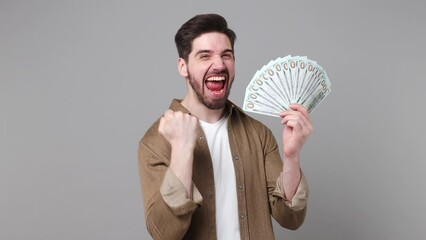 Sticker - Young exultant caucasian man 20s he wear brown shirt hold in hand stack of cash money in dollar banknotes do winner gesture isolated on plain grey background studio portrait. People lifestyle concept