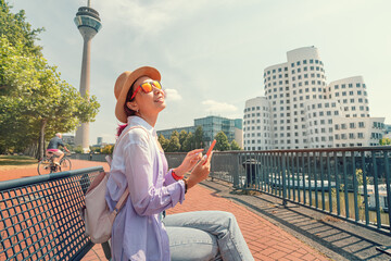 Wall Mural - A girl traveler with smartphone enjoys a beautiful view in the Media Bay harbor and TV Tower during a tourist trip or a student education in Dusseldorf, Germany