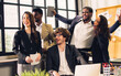 © Ann Rodchua - Group of diverse multiethnic businesspeople wearing formal suits, raising hands, smiling together with happiness and success, standing in modern indoor office after finishing teamwork project.