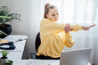 © irissca - Workout at work. Office Exercises at desk, Desk Friendly Workplace Exercises To Keep Healthy at Office. Young woman office worker at her workplace stretching hands and body taking break from work