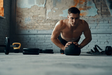 Wall Mural - Concentrated young man using medicine ball while doing push-up exercises in gym