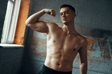 Wall Mural - Confident muscular man showing his perfect bicep while standing in gym