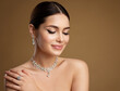 Beauty Model in Wedding Jewelry Set. Elegant Woman in Necklace with Earring and Ring. Beautiful Girl with perfect Eyeliner Make up and smooth Skin over Beige Background