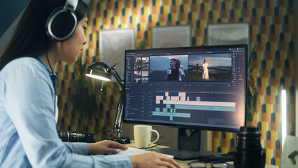 Wall Mural - concentrated asian woman sitting at the table and editing video for client in professional software 