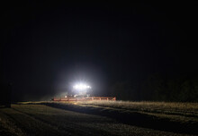 Combine Harvester Working At Night With Front Headlights Illuminating The Field During The Last Days Of Harvesting Season
