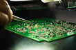 Manual assembly of electric components onto green PCB. Closeup shot of a hand of unrecognizable caucasian man holding tweezer-like tool and glueing electric pieces onto printed circuit board. High