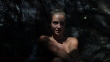 Smile Of A Naked Pretty Woman With Blue Eyes And Blonde Hair In Front Of A Waterfall. Slow Motion