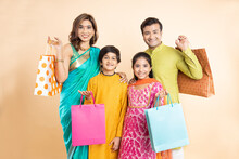 Portrait Of Happy Indian Family Wearing Traditional Cloths Holding Shopping Bags And Celebration Diwali Festival Together Isolated On Studio Background. Parents With Kids Celebrate Festive Season Sale