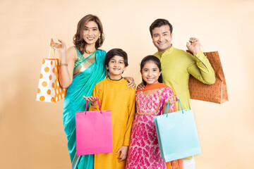 Portrait of Happy indian family wearing traditional cloths holding shopping bags and celebration diwali festival together isolated on studio background. Parents with kids celebrate festive season sale