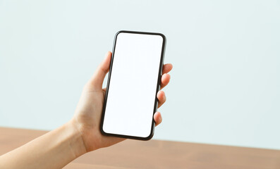 Wall Mural - Hands holding smartphone with mockup of blank screen on sofa in living room.