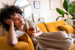 © Daniel - Happy African American woman relaxing at home lying on couch holding cup of warm coffee looking at camera. Copy space.
