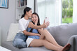 © amenic181 - Happy young Asian lesbian couple taking selfie in the living room. LGBT couple lifestyle concept.