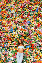 Smiling Woman With Arms Outstretched Standing In Front Of Multi Colored Flower Wall