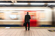 © Westend61 - Senior passenger with laptop bag standing in front of speeding train on subway platform