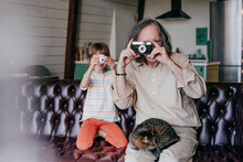 Grandfather With Vintage Camera And Granddaughter With Toy Camera Taking Photos At Home